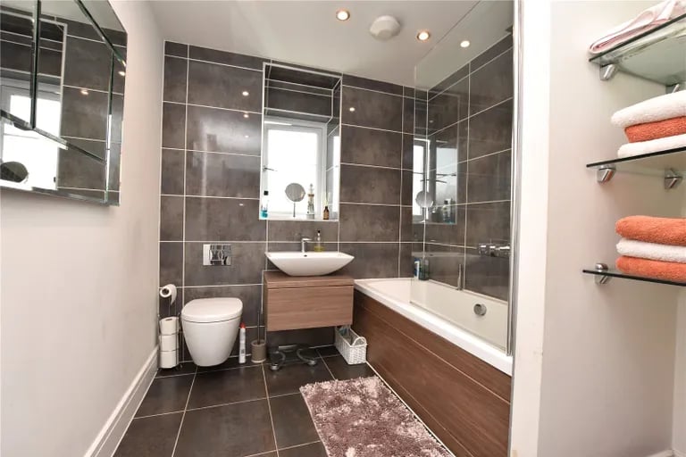 The contemporary house bathroom has a three-piece suite with shower facilities and screen over the bath.