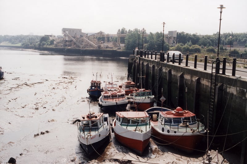 Photograph of some small boats lying in silt and docked by the quayside with Gateshead Gravel works in the background across the Tyne.