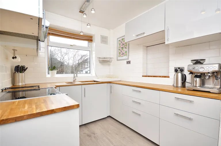 The modern bright kitchen has a serving hatch into the dining area, fitted base and wall units and large work surfaces.
