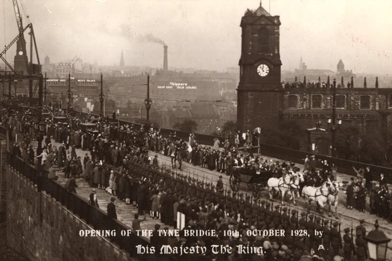 A postcard commemorating the opening of the Tyne Bridge Newcastle upon Tyne by George V on 10 October 1928. The photograph shows a procession led by the King's carriage which has crossed the bridge into Gateshead. A crowd has gathered on the bridge to watch the procession. All Soul's Church is to the right of the bridge.The Tyne Bridge was designed by Mott Hay and Anderson and was constructed between 1924 and 1928. 