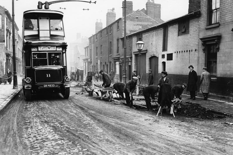 circa 1923:  A 'trackless tram' trolley bus in Birmingham, passing workmen pulling up the old track line.  (Photo by Topical Press Agency/Getty Images