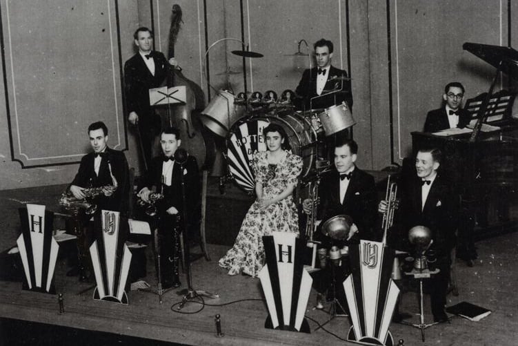 The band is pictured playing at a Jazz Jamboree in Airdrie Town Hall. Back row (l-r): Fred Hope (bass), Bill Downie (drums), and Tom Pearson (piano) Front row (l-r): Pat Kelly (tenor sax), Bobby Gillespie (alto saxophone), Mary Scanlon (singer), Bob Letham (trumpet) and Sam Grant (trumpet).