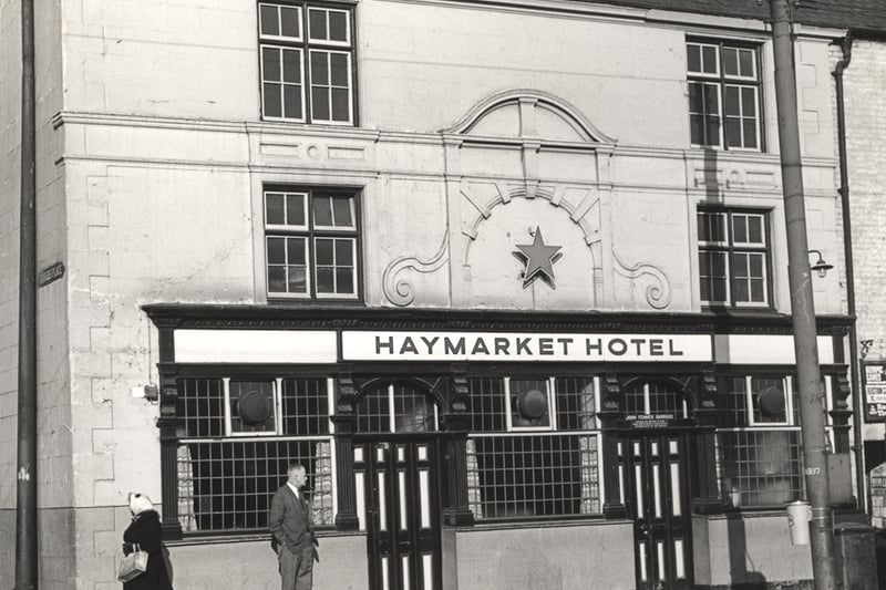 The photograph shows the frontage of the Haymarket Hotel in 1964. An elderly woman has just walked past a man who is standing outside the pub.