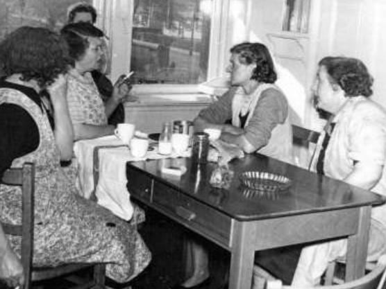A group of cleaners crowd round a table after a shift for a cup of tea, a cigarette, and a gossip.