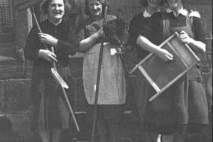 A group of women pose with household items outside a tenement in Partick