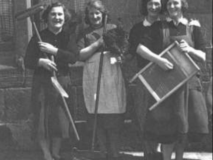 A group of women pose with household items outside a tenement in Partick