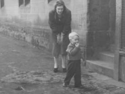 A young mother watches her well-dressed toddler saunter around outside the front steps