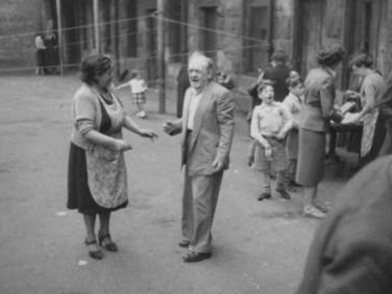 A group of men, women and children look like their having a grand time during a jumble sale in a Partick back court