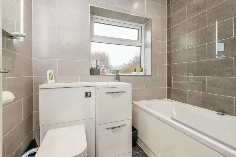 The tiled bathroom features a WC and bathtub with shower over.
