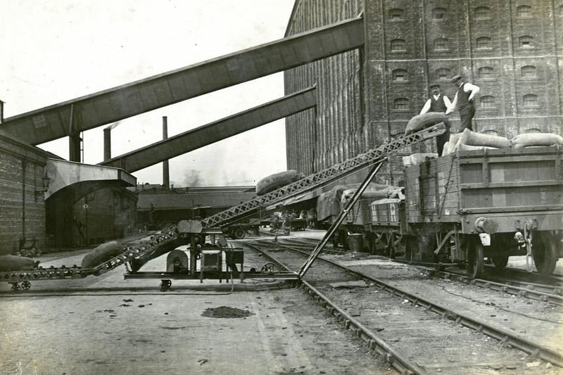 Working Partick men load sacks of grain on to a railway wagon using a motorised conveyor belt. 