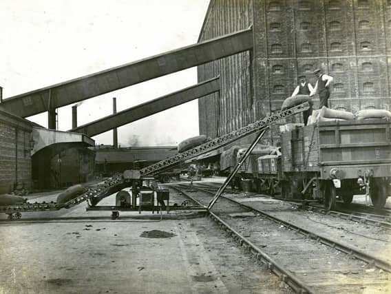 Working Partick men load sacks of grain on to a railway wagon using a motorised conveyor belt.