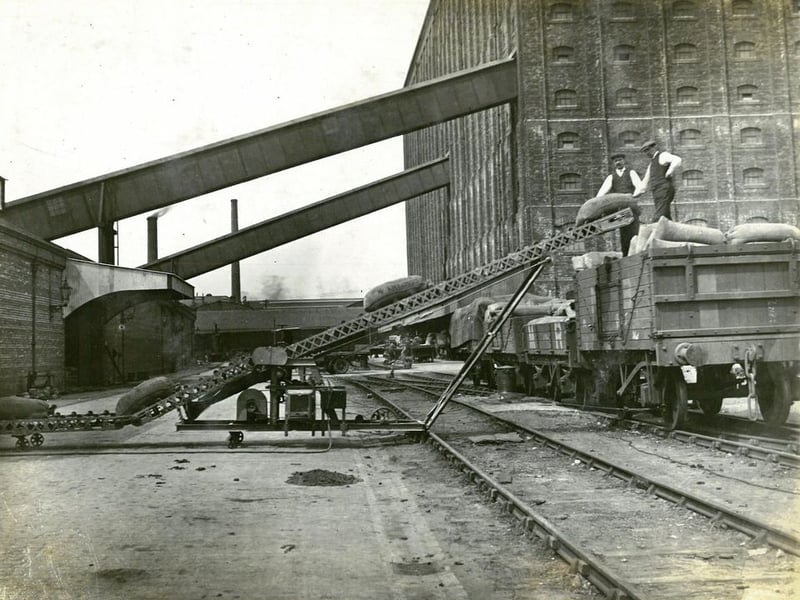 Working Partick men load sacks of grain on to a railway wagon using a motorised conveyor belt.