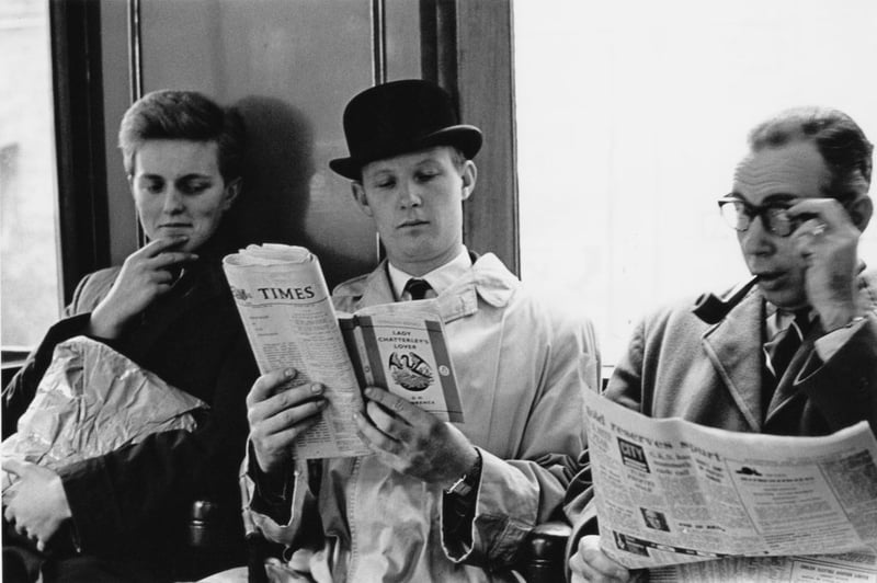 On the London Underground a commuter reads a copy of D H Lawrence's 'Lady Chatterley's Lover', unaware of the fellow passengers surreptitiously reading over his shoulder.