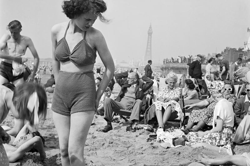 A young woman in a knitted bathing costume stands on the beach in the midst of the crowds of holidaymakers, Blackpool, c1946-c1955. Blackpool Tower is visible in the background. (Photo by English Heritage/Heritage Images/Getty Images)