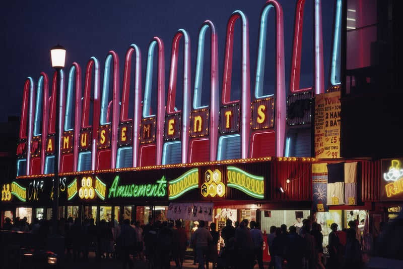A night view of holiday makers walking along the Golden Mile which is illuminated by neon signs for amusements in the seaside town of Blackpool, Lancashire, April 1987.  (Photo by RDImages/Epics/Getty Images)