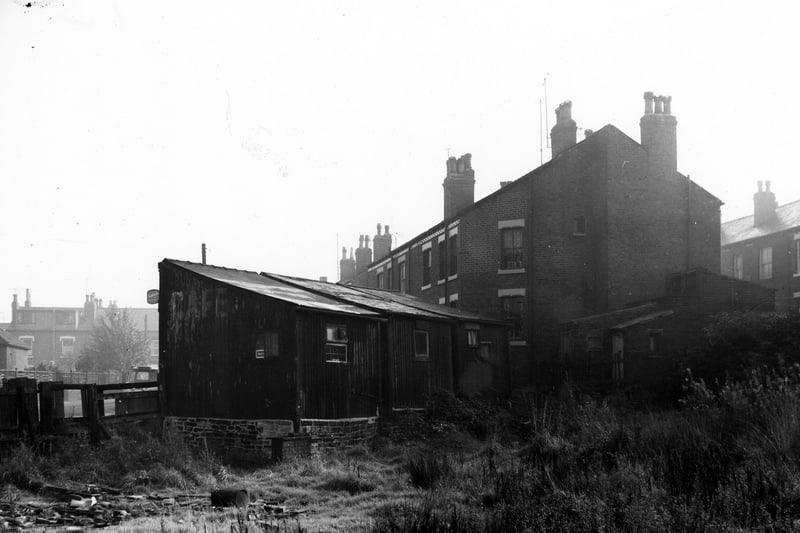 This view looks across wasteland onto properties on Cow Close Road. In the centre are three one-storey buildings seen from the back, these are numbers 47 to 43. Cow Close Road continues in the background with Wilfrid Street just visible on the right edge.