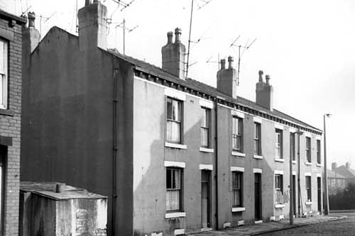 looks along back-to-back properties on Wilfrid Terrace in the direction of Branch Road. Houses are cement rendered and numbers run from 8 to 2, left to right. Several television aerials are visible on the roof.