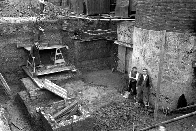 the foundation work in progress on the new committal chamber in the Cottingley Hall Crematorium. Workmen can be seen working on the site. Wooden planks, spades and wooden framework can all be seen. Pictured in September 1953.