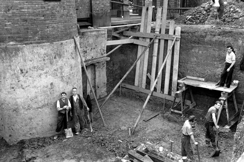  foundation work in progress on the new committal chamber at Cottingley Hall Crematorium. Wooden supports hold up the side of the pit and workmen with shovels look at the camera. Pictured in September 1953.