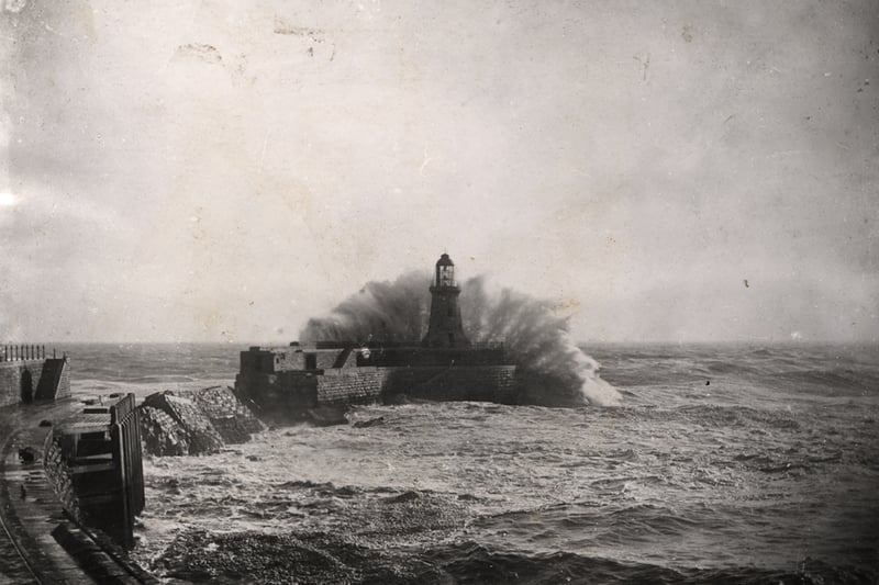 A view of Tynemouth lighthouse and pier Tynemouth taken in c.1905. Waves are crashing against the pier. The breach in the curve of the pier caused by a storm can be seen. The pier was rebuilt without a curve and was completed in 1909.