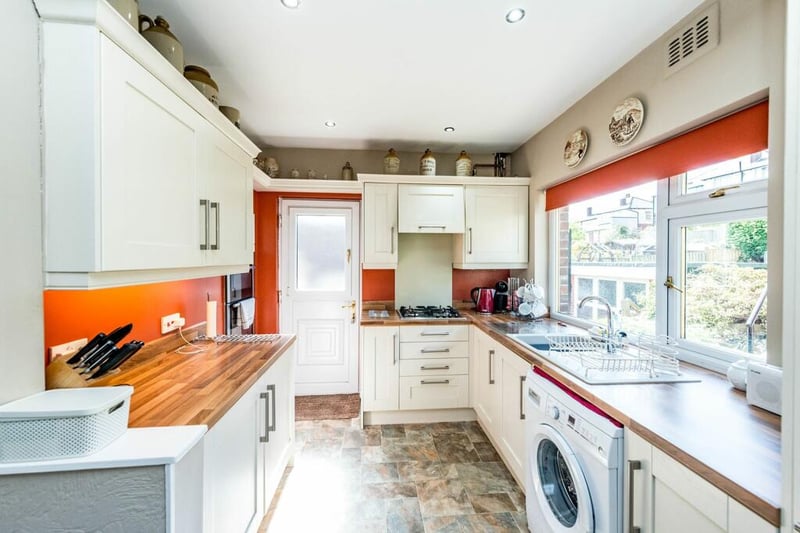 The kitchen has a pop of colour in the way of orange walls and blinds, and looks out onto the garden.