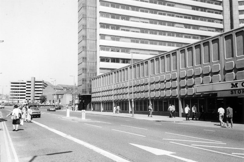 Woodhouse Lane showing Morrisons supermarket with the office block Merrion House towering above. These were both completed in 1972 as an addition to the Merrion Centre, the initial part of which had opened in 1964. Further along is the junction with Clay Pit Lane then on the left the Woodhouse Lane multi-storey car park can be seen. 
