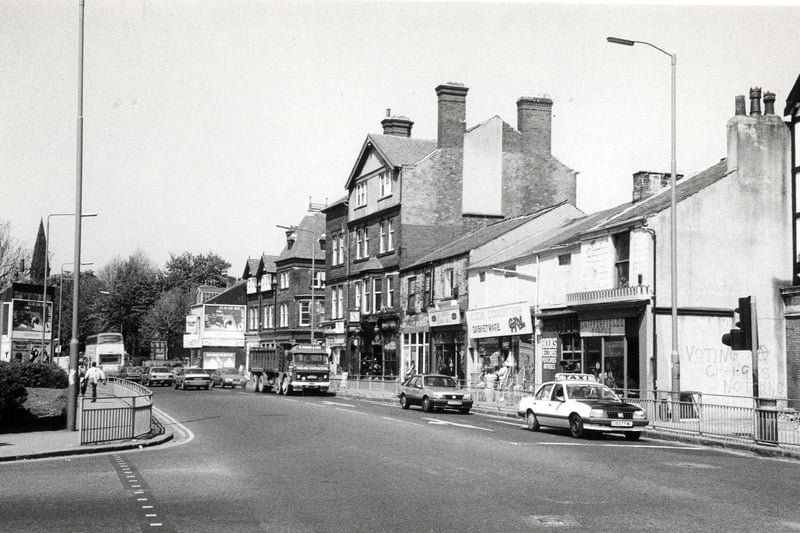 Looking north-west along Headingley Lane from Hyde Park Corner. The junction with Hyde Park Road is on the left. On the far right is the edge of The Hyde Park public house. Shops following on from this include Snipperfields Circus hairdressers, a cane furniture and basketware store and La Paprika coffee bar.