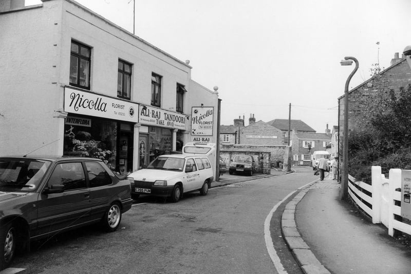looking north-west along Bank Street showing Nicolla, Florist, on the left at no. 1 followed by Ali-Raj Tandoori takeaway at no. 3. Further along is Write Printers and Stationers which faces onto Church Street where it is numbered 13.