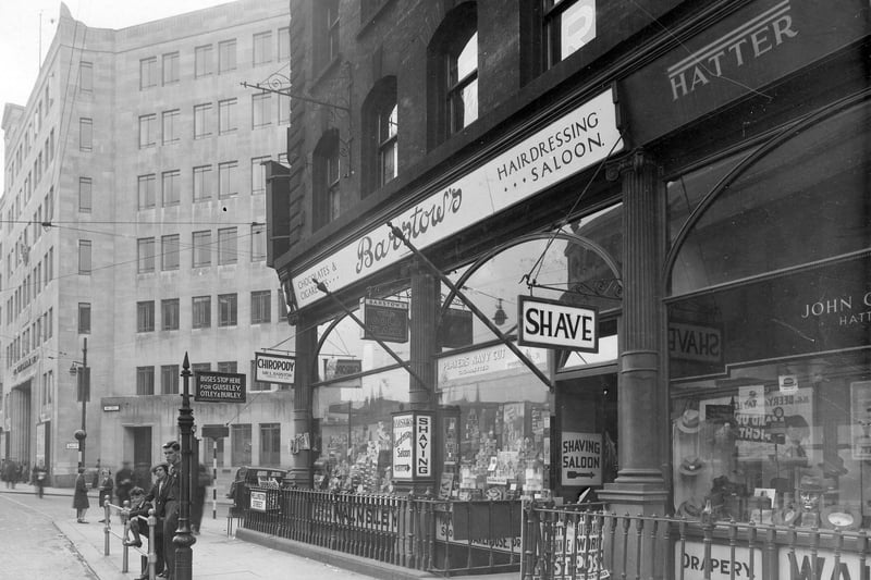 Wellington Street in June 1939 which includes, Barstow's confectioners and tobacconists, W Barstow's haridressing/shaving saloon and L Barstow chiropody. There are barber's poles. The shop has a double window with displays of confectionery in one and pipes and tobacco in the other. Next door (also number 11) John Craig's Hatters, with a window display of men's hats including trilbys. Walmsley's drapers etc of Wellington Chambers takes up the cellar space. Across Aire Street is Leeds Joint Railway Station and the Queens Hotel.