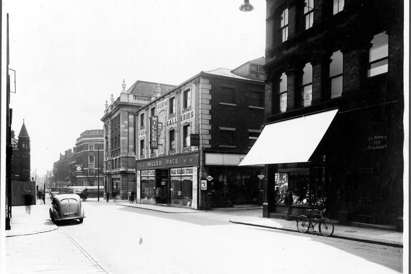 Albion Street, looking south to Boar Lane across The Headrow in August 1939. Number 125, St Ann's Buildings housed Hillman Brothers wireless factors, Leeds Premier Supply Co. clothing club, Miss Lizzie Crosby artist, Loyal Order of Ancient Sheperds Friendly Society. At the top of the building, sign 'Hearts of Oak' Assurance Co. Ltd. number 123 S.N. Kilner jeweller has shop blind down to protect window. Next, junction with Coronation Place. Number 119 Miller Page Furnishing. There is a hanging sign on shop front and banners in the window inform that it is a 'Walk Round Store' Junction with Upper Fountaine Street. Corner of 44 to 68 Headrow building used as Tax offices, Electricty Offices. Directly across the Headrow (with clock) number 105 Albion Street is the Leeds and Holbeck Building Society.