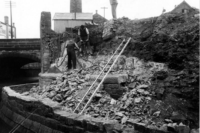 Work on a new retaining wall for Sheepscar Beck near Sackville Street. Some workmen stand on the banking, one is using a pneumatic drill. An arched bridge is to the left, with a workman's hut on top. A ladder is in the foreground.. Pictured in September 1949.