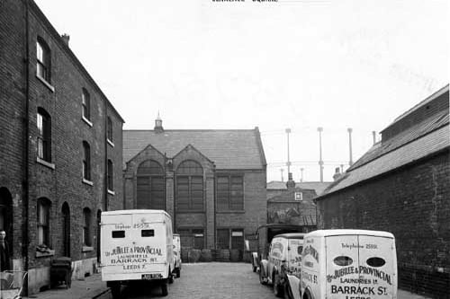 This view looks south-west down Clarence Square at the rear of Sheepscar Congregational Chapel. In the foreground are several vans from The Jubilee & Provincial Laundries Ltd., on Barrack Street. In the distance a gasholder is visible. Pictured in October 1946.