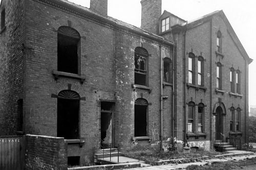 Derelict houses off Camp Road. House to right has 3 storeys and a dormer window with arched lintels above each window. The houses on the left have broken windows. There is a metal dustbin outside one house. Pictured in July 1945