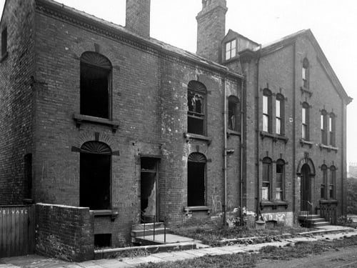 Derelict houses off Camp Road. House to right has 3 storeys and a dormer window with arched lintels above each window. The houses on the left have broken windows. There is a metal dustbin outside one house. Pictured in July 1945