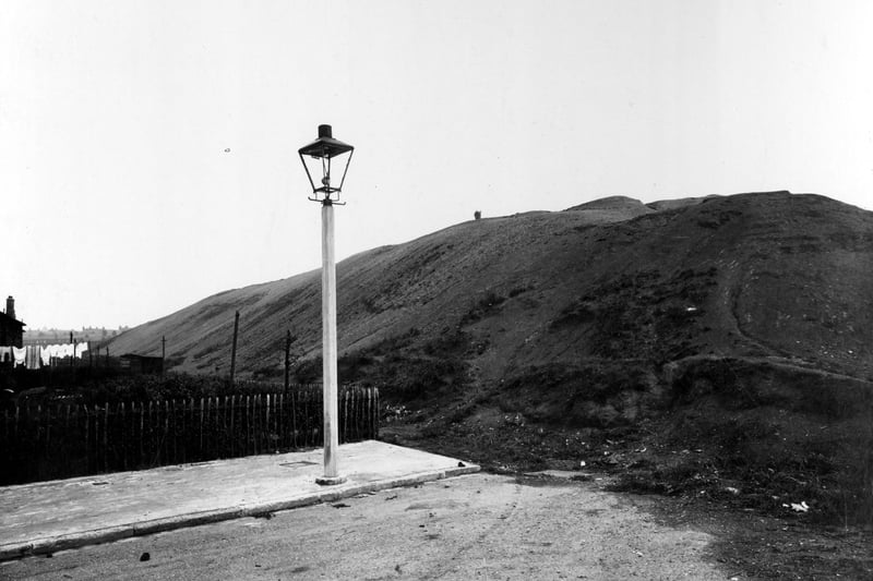 Gas lamp post at the end of a path. To the right is a large mound of earth on the edge of the York Road pits. A line of washing is out in the garden of the house to the left. Pictured in September 1938.