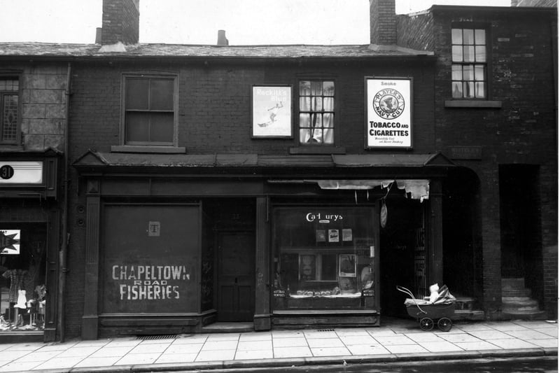33 Chapeltown Road, the premises of 'R. Hall, Fried Fish Dealer. Next door is a newsagents with 'Cadburys', 'Nutalls Mintoes', 'Persil' and 'Puritan Soap', all advertised in the window. A sign above the shop says, 'Players Navy Cut, Tobacco and Cigarettes'. Whitley Court is visible to the right of the photo. A baby is sat in a pram looking into the shop in the foreground. Pictured in July 1948
