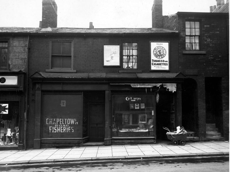 33 Chapeltown Road, the premises of 'R. Hall, Fried Fish Dealer. Next door is a newsagents with 'Cadburys', 'Nutalls Mintoes', 'Persil' and 'Puritan Soap', all advertised in the window. A sign above the shop says, 'Players Navy Cut, Tobacco and Cigarettes'. Whitley Court is visible to the right of the photo. A baby is sat in a pram looking into the shop in the foreground. Pictured in July 1948