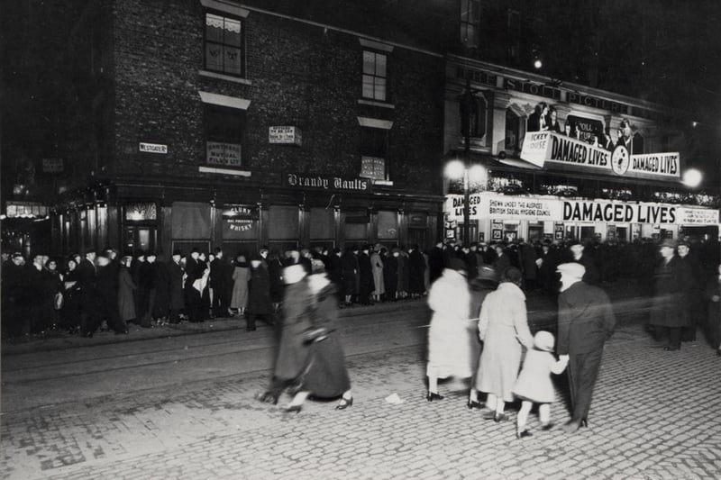 A view of the Stoll cinema Westgate Road Newcastle upon Tyne taken in 1934. The photograph shows people queuing outside the Stoll to see the film 'Damaged Lives'. The 'Brandy Vaults' pub is to the left of the Stoll. 'Damaged Lives' was a film about the effects of V.D.