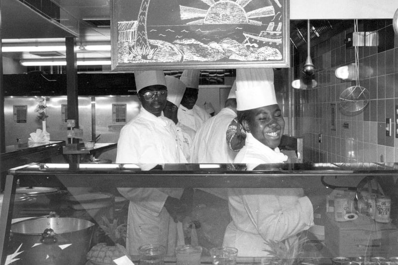 Staff behind the counter of Dr. B's Caribbean restaurant in December 1989. It was set up by Doctor Barnado's, the young people's charity. The restaurant was run with funding from Task Force, the Home Office and Leeds City Council. The 36 seater venue provided young people with City and Guilds, Caterbase Hotel and Catering Training Board qualifications over two years, and they were paid YTS training allowances. The restaurant proved very popular for its traditional dishes of Caribbean chicken, steamed fish with cornmeal, stuffed cheese aubergine, served with gunga peas and rice, leaks, plantain and roast potatoes. The successful scheme continues today with around 70 per cent of the young people trained finding work in the catering industry. The large, red brick restaurant opens for lunch from Tuesday to Friday.