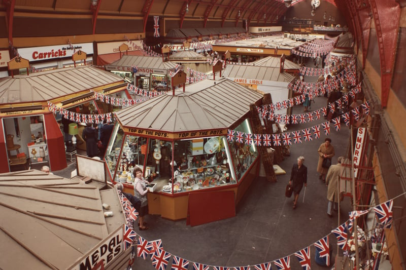  A view of the interior of the Grainger Market Newcastle upon Tyne taken in 1977. The photograph has been taken from one of the balconies inside the hall and is looking down onto the stalls and shops. The hall has an iron and glass roof. The buildings is decorated with flags and bunting for the Silver Jubilee of Queen Elizabeth II.
