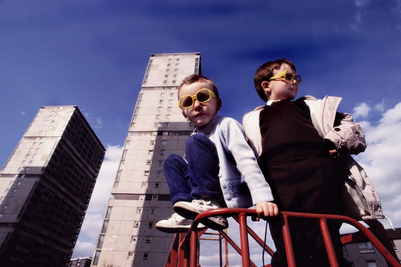Children wearing yellow sunglasses playing outside their block of flats in 1990.