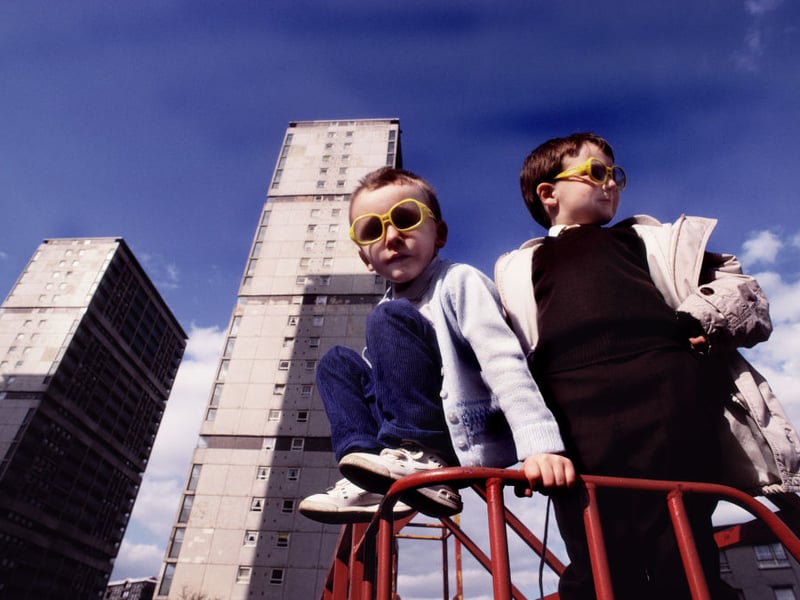 Children wearing yellow sunglasses playing outside their block of flats in 1990.