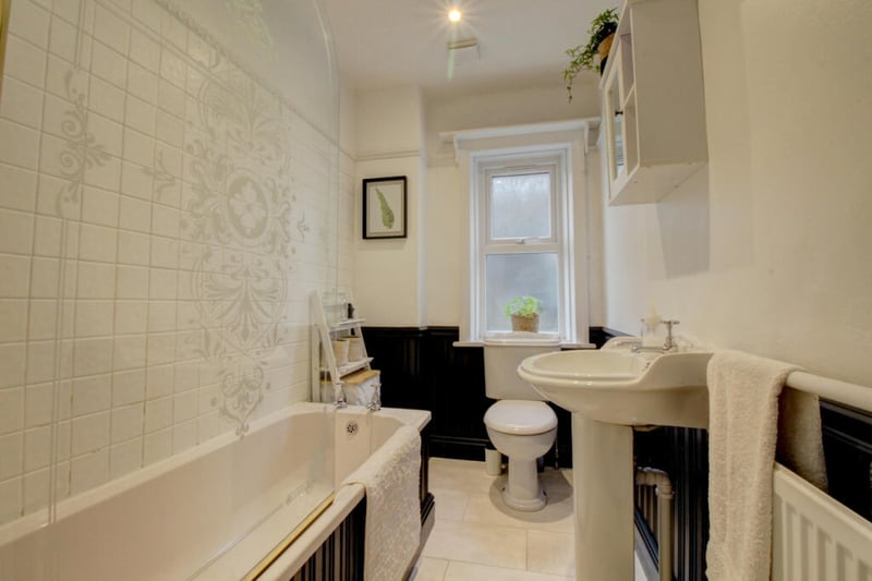 The house bathroom has a stained glass door and offers a panelled bath with shower over.