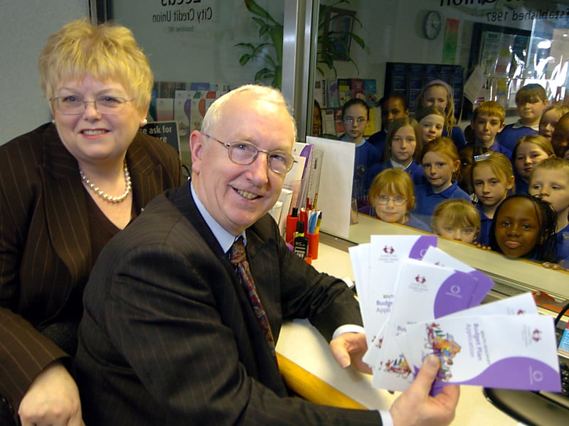 Leeds East MP George Mudie and Susan Davenport, chief executive-Leeds City Credit Union, behind the counter at the opening of the new Leeds City Credit Union branch at Seacroft South One Stop Centre in March 2006. Looking on are children from Seacroft Grange Primary choir who entertained at the opening ceremony.