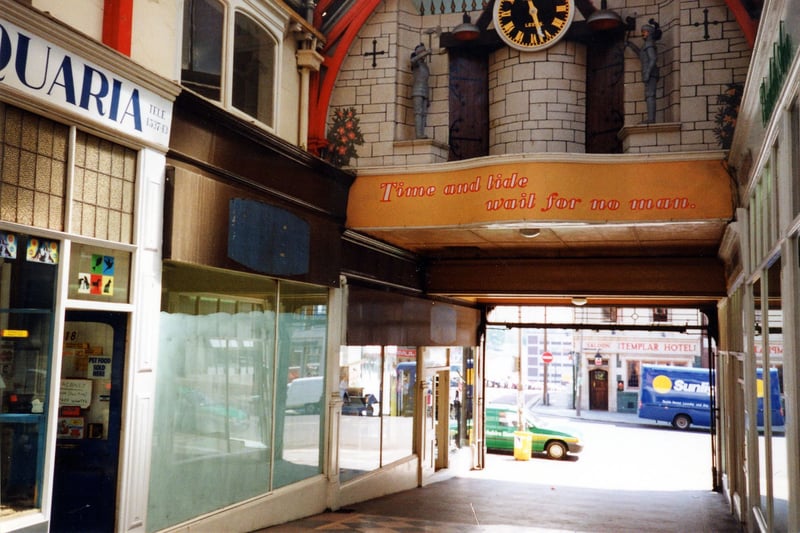 A view looking out from the Grand Arcade at the Vicar Lane entrance. On the left is no.18-19, Pets and Aquaria, which has been in business in the Grand Arcade since 1940. Above the entrance is the Potts Mechanical Clock built in 1898, with the motto 'Time and tide wait for no man'. Across the road on Vicar Lane the Templar Hotel can be seen. Pictured in October 1990.