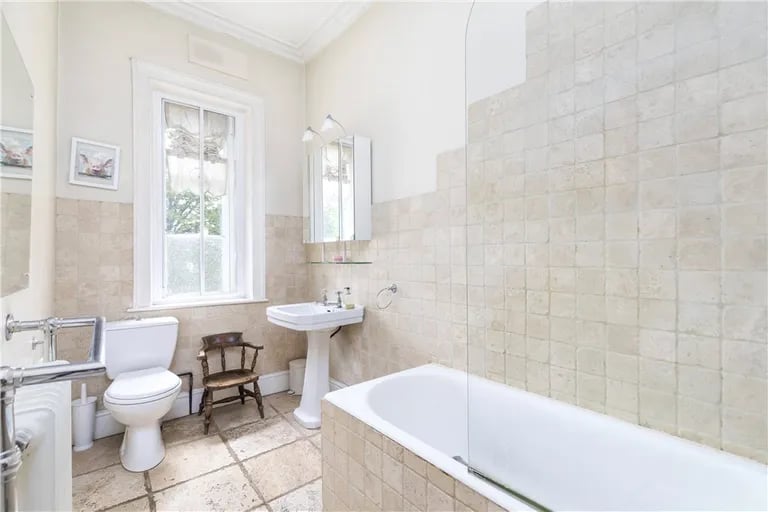 The tiled house bathroom has a bath with shower over.