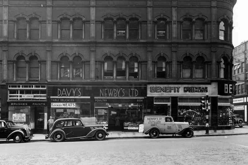 shops on The Headrow and the junction with Lands Lane at the right edge in September 1938.. Pictured, from left, are West Riding Wallpapers at number 61A, which is shortly to open, Arthur Davy & Sons Ltd. provision merchants, specialising in 'table delicacies', cooked meats, pies and sausages at number 63, Newby's Ltd., fish, game and poultry salesmen at number 65 advertising 'Herring Week' and 'Herring for Health' as well as 'fresh boiled salmon' and 'choice roast turkey'. Newby's van is parked in front of the shop. At number 69 is Benefit Footwear Specialists on the corner with Lands Lane.