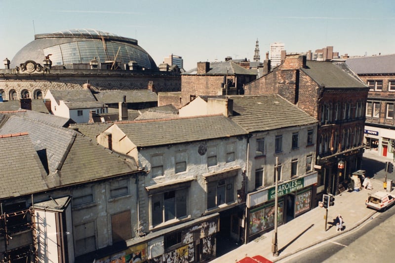 Kirkgate in October 1990. On the left, No's.101-103 are vacant and boarded up, with scaffolding above and fly posters covering the windows. Next door to these No.104, Carole's childrenswear, is advertising a sale. On the corner by the junction with Call Lane, is the Scotsman public house at No.1 Call Lane. Across the road, No.2 Call Lane, Henry Brown Electrical Ltd is just visible. The dome of the Corn Exchange can be seen in the background.
