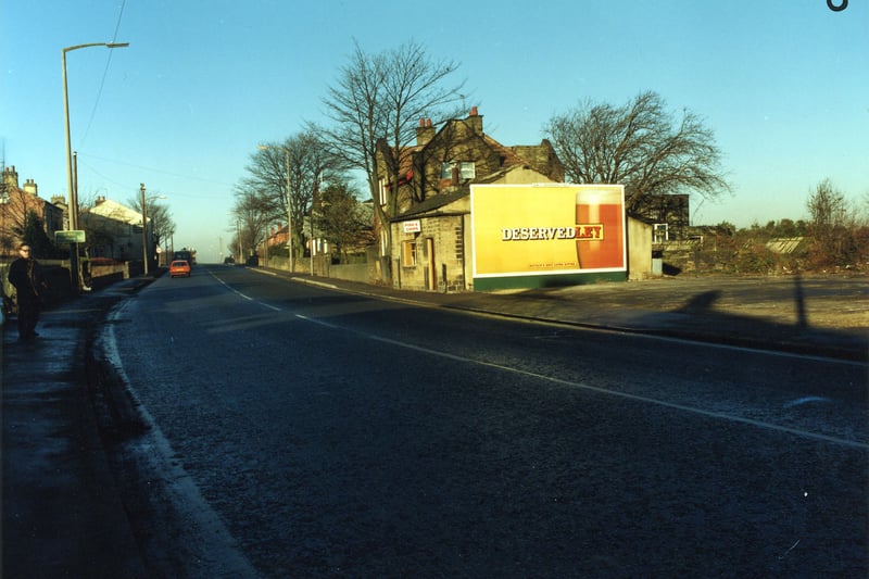  looking north-west along Bradford Road, showing a fish and chip shop at no. 28 in the centre, with a large advertisement for Tetley's Bitter on the side. Further along the road is the Tempest Constitutional Club, and on the left hand side, the white building is the Painter's Arms public house. Pictured in December 1990.