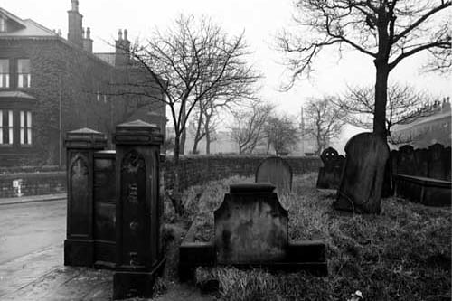 This photo shows part of the graveyard belonging to St Bartholomew's Church on the corner with Church Road and Strawberry Lane. The main entrance is visible in the foreground but the gate is no longer there. Houses and trees are visible. Pictured in December 1947.